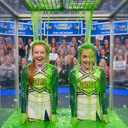 Two middle school cheerleaders,. Both have their hair in tight ponytail tied with ribbon and held. One has straight ginger hair, the other light brown hair. Looking directly at viewer, with giggling little smiles. Close shot.